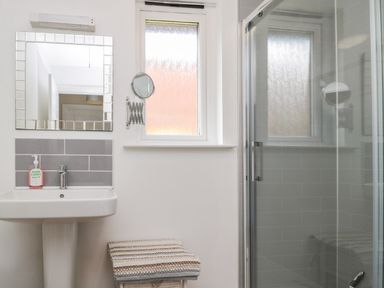 A bathroom with a sink a mirror a window a shower enclosure and a basket with towels at The Shieling in Warkworth