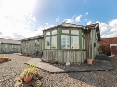 Exterior view of a wooden house with green window frames and potted plants on a gravel yard at The Shieling in Warkworth