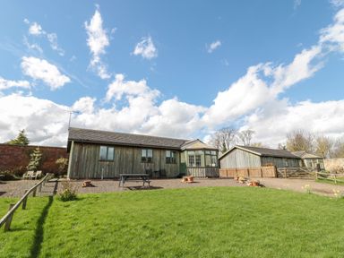 A wooden house with a fenced garden and picnic bench under a blue sky at The Shieling in Warkworth