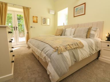 A bedroom with a bed with pillows a chest of drawers and glass doors with curtains at Langdale Barn in Sampford Courtenay