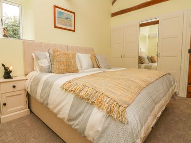 A bedroom with a bed a bedside table with a lamp a wardrobe and a painting on the wall at Langdale Barn in Sampford Courtenay