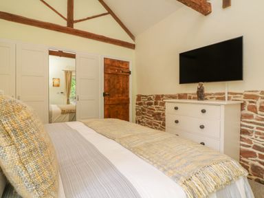 A bedroom with a bed and a dresser with a television mounted above at Langdale Barn in Sampford Courtenay