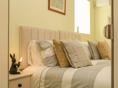 A bedroom with a beige upholstered headboard pillows on a bed and a nightstand with a rabbit lamp at Langdale Barn in Sampford Courtenay