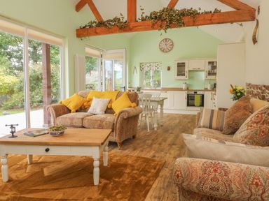 A sitting area with upholstered sofas yellow cushions wooden coffee table and a kitchen in the background at Langdale Barn in Sampford Courtenay