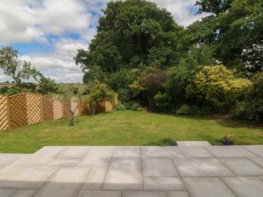 A backyard with a stone patio grass lawn wooden fence and trees at Langdale Barn in Sampford Courtenay