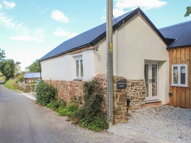 A stone and plaster house with a gravel driveway next to a road at Langdale Barn in Sampford Courtenay