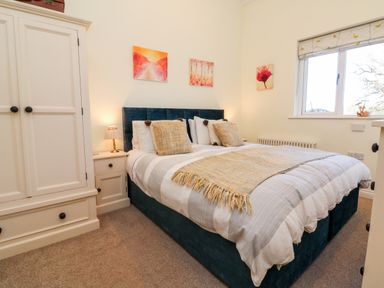 A bedroom with a double bed nightstands lamps wardrobe and paintings on walls at Langdale Barn in Sampford Courtenay