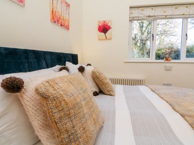 A bedroom with a bed featuring striped bedding and knitted pillows near a window with patterned blinds at Langdale Barn in Sampford Courtenay