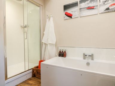 A bathroom with a bathtub, glass shower enclosure, white towels hanging on hooks, and pictures of boats above the tub at Langdale Barn in Sampford Courtenay
