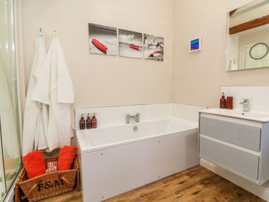 A bathroom with a bathtub white robes on hooks and a basket with towels at Langdale Barn in Sampford Courtenay