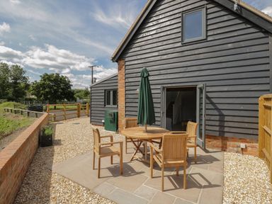 An outdoor patio area with a wooden table and four chairs and an umbrella attached to the table at Kingfisher 2 The Old Stables Witney