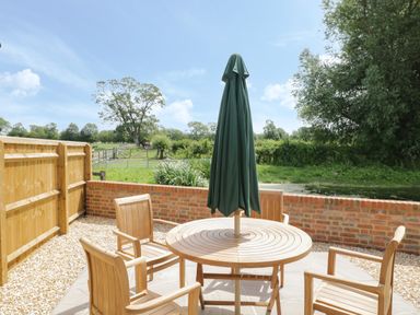 An outdoor patio with wooden table and chairs and a closed umbrella surrounded by a brick wall and a wooden fence at Kingfisher 2 The Old Stables Witney