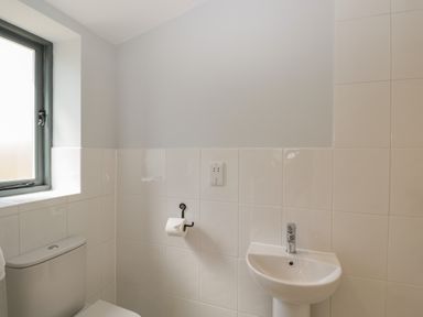 A bathroom with a toilet, a sink, a window, and a toilet paper holder at Kingfisher 2 The Old Stables in Witney