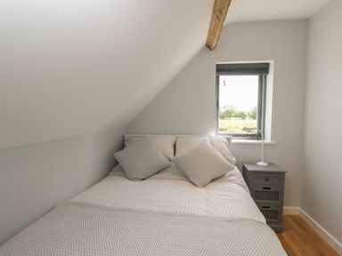 A bedroom with a bed two pillows a bedside table with a lamp and a window at Kingfisher 2 The Old Stables in Witney
