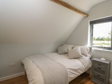 A bedroom with a bed beside a window and a small bedside table with a lamp at Kingfisher 2 The Old Stables in Witney