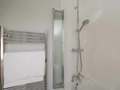 A bathroom with a metal towel rack holding a white towel next to a bathtub with a showerhead at Kingfisher 2 The Old Stables in Witney