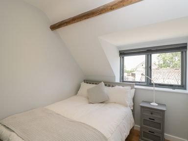 A bedroom with a bed next to a window and a bedside table with a lamp at Kingfisher, 2 The Old Stables in Witney