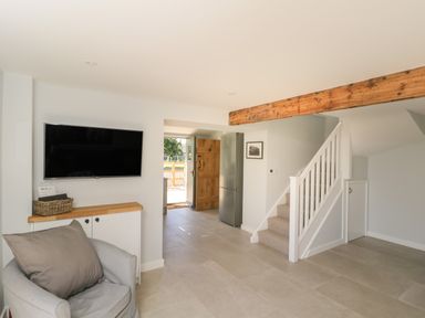 A living room with a gray armchair a mounted TV wooden beam and a staircase at Kingfisher 2 The Old Stables in Witney