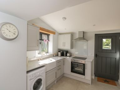 A kitchen with white cabinets a washing machine an oven and a black door at Kingfisher 2 The Old Stables in Witney