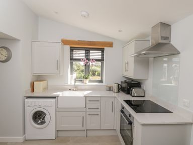 A kitchen with a washing machine sink stovetop oven and window with flowers at Kingfisher 2 The Old Stables in Witney