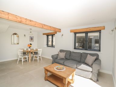A living room with a gray sofa a wooden coffee table and a dining table with white chairs at Kingfisher 2 The Old Stables in Witney