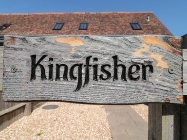 A wooden sign with the word Kingfisher carved into it mounted on a fence outdoors at Kingfisher 2 The Old Stables Witney
