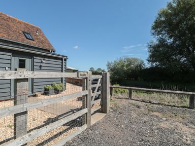 A wooden gate and fence outside a building with a gravel pathway and trees in the background at Kingfisher 2 The Old Stables Witney