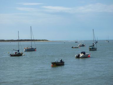 Several boats anchored on calm water with a sandy shore and low vegetation in the background at The Look Out in Aberdovey