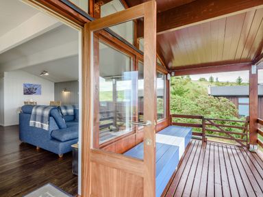 A wooden deck with blue and white bench seats leading to a living room with a blue sofa and dining table at The Look Out in Aberdovey