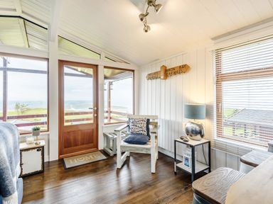 A wooden chair with pillows near a wooden door with windows and a side table with a lamp in a room at The Look Out in Aberdovey