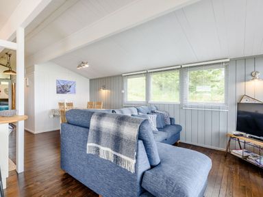 A living room with blue sofas, a television on a wooden stand, and a dining table with chairs at The Look Out in Aberdovey