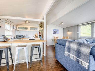 An open plan kitchen and living area with stools at a counter a blue sofa and a dining table at The Look Out in Aberdovey