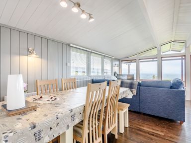 A dining area with wooden chairs and a living room with blue sofas and large windows at The Look Out in Aberdovey