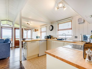 A kitchen with wooden countertops and white cabinets next to a living area with a blue sofa at The Look Out in Aberdovey