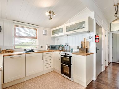 A kitchen with white cabinets wooden countertops a stove and a window with blinds at The Look Out in Aberdovey