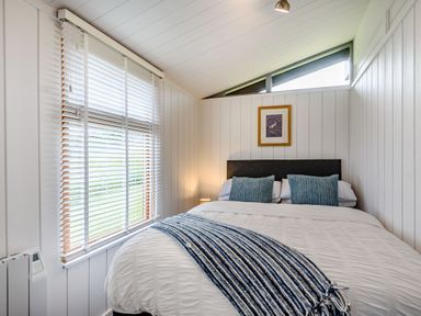 A bedroom with a bed and blue pillows and a striped blanket next to a window with blinds at The Look Out in Aberdovey