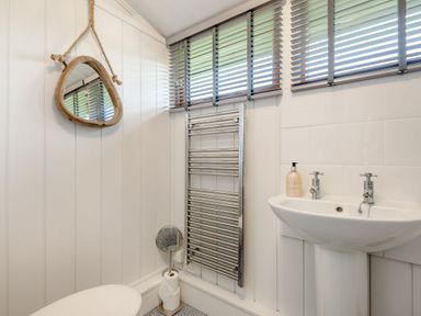 A bathroom with a toilet sink a towel radiator a rope hanging mirror and window blinds at The Look Out in Aberdovey
