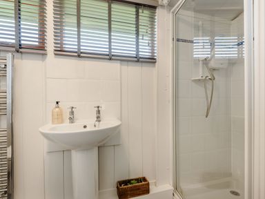 A bathroom with a pedestal sink a shower with glass door and window blinds at The Look Out in Aberdovey