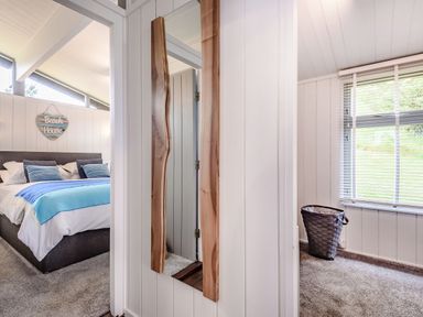 A bedroom with a bed a wall mirror and a laundry basket near a window at The Look Out in Aberdovey