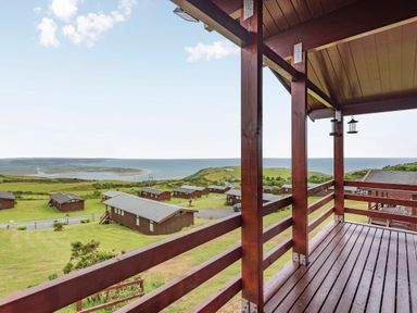 A wooden balcony overlooking a grassy area with several wooden cabins near the coast at The Look Out in Aberdovey