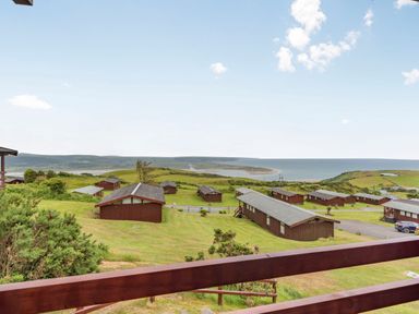 A view of wooden cabins on a grassy hill overlooking a coastline at The Look Out in Aberdovey