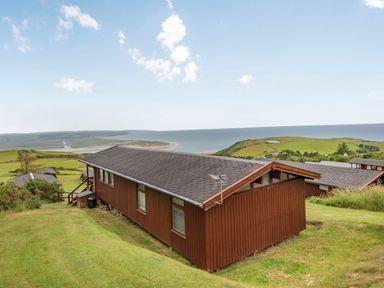 A brown wooden house on a grassy hill overlooking a coastline and ocean at The Look Out in Aberdovey