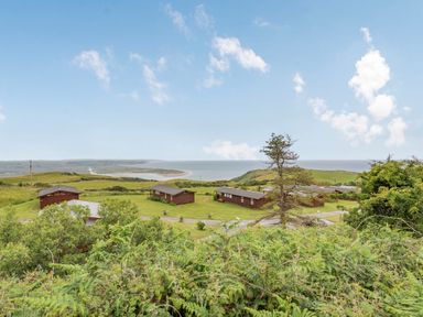 A view of wooden cabins on grassy land with ocean and hills in the background at The Look Out in Aberdovey