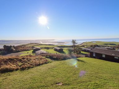 A grassy hillside with several cabins and a view of the sea at The Look Out in Aberdovey