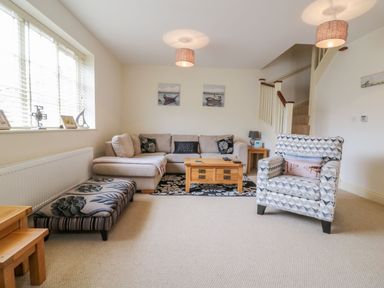 A living room with a sectional sofa armchair coffee table and staircase at 26 Burtons Mill in Stalham