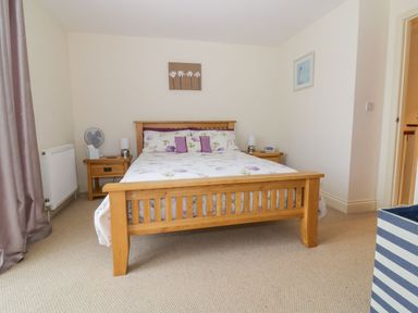 A bedroom with a wooden bed with floral bedding and two wooden bedside tables at 26 Burtons Mill in Stalham