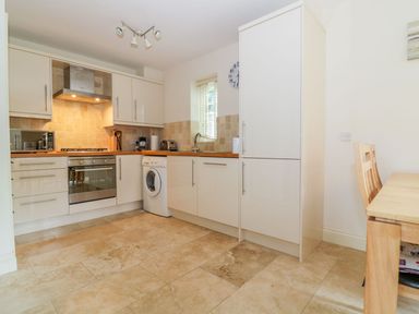A kitchen with white cabinets a washing machine a microwave an oven and a dining table with chairs at 26 Burtons Mill in Stalham