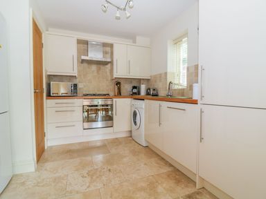 A kitchen with white cabinets a washing machine a microwave a toaster and a stove at 26 Burtons Mill in Stalham