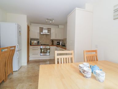 A kitchen with wooden chairs a refrigerator and a dining table with mugs and a teapot at 26 Burtons Mill in Stalham