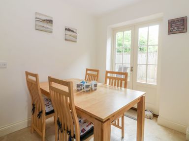 A dining room with a wooden table and four chairs near glass doors at 26 Burtons Mill in Stalham